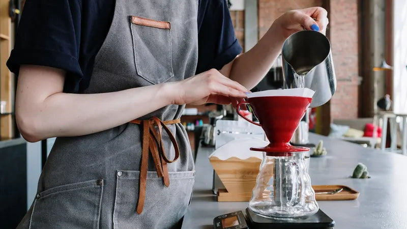 Önlüklü bir baristanın kafe tezgâhında tartı üstünde V60 ile filtre kahve demlemesi